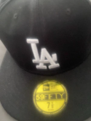Svart LA New Era 59FIFTY keps - Säljer en svart New Era 59FIFTY keps med LA-logga broderad framtill i vitt och klassisk rak skärm. Kepsen har New Era-loggan på sidan och är i ett tåligt material som passar perfekt till streetwear-stilen.