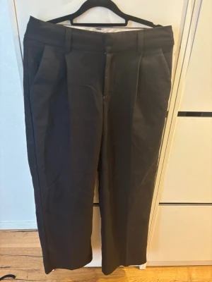 Svarta raka kostymbyxor - Snygga svarta kostymbyxor med raka ben och pressveck. Byxorna har hällor för skärp, sidofickor och en bakficka. Perfekta för en clean och stilren look. Materialet ser ut att vara en klassisk kostymblandning som ger en dressad känsla.