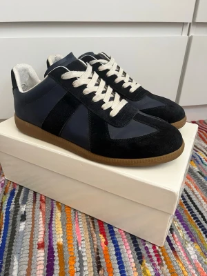 Navy Maison margiela Gats sneakers - Snygga sneakers i marinblått med kontrasterande vita/beiga skosnören och gummisula. Ovandelen kombinerar mocka och slätt läder material för en stilren look. Insidan är vit och sulan har en klassisk brun färg. Perfekta för dig som gillar minimalistisk och tidlös stil. Skriv vid funderingar priset är inte fast!