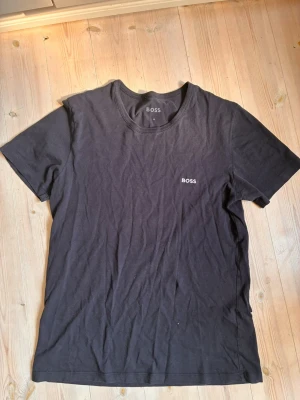 Svart t-shirt från BOSS - Snygg svart t-shirt från BOSS med diskret logga på bröstet. Klassisk rund halsringning och korta ärmar. Perfekt basplagg i mjuk bomull som funkar till allt. Enkel och stilren design som alltid är rätt.