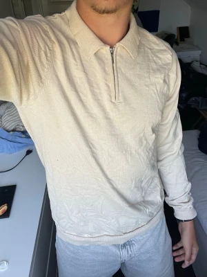 Beige ziptröja från Harry Brown - Snygg beige långärmad tröja från Harry Brown med halv dragkedja och klassisk krage. Tillverkad i mjukt stickat material som ger en clean och stilren look. Perfekt för dig som gillar minimalistisk stil och neutrala färger.