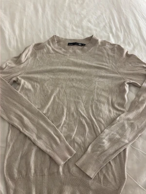 Beige tunn stickad tröja - En enkel och stilren beige stickad tröja med rund halsringning och långa ärmar. Tröjan är tunn och har ribbade muddar vid ärmslut och nederkant. Perfekt att matcha med jeans eller kjol för en clean look. OBS! har två små hål i båda armhålorna efter mycket användning och tvättning.