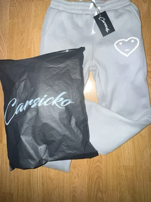 Grå carsicko tracksuit  - Säljer ett par grå mjukisbyxor från Carsicko med ett vitt broderat hjärta och stjärnögon på ena benet. Byxorna har dragsko i midjan och resår vid bensluten. Perfekta för en chill och avslappnad stil.skriv för mer bilder.