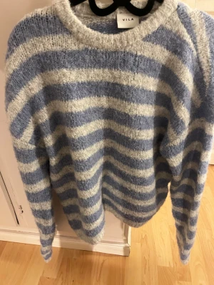 Blåvit randig stickad tröja Vila - Smygg och mysig stickad tröja från Vila med breda horisontella ränder i ljusblått och vitt. Tröjan har rund halsringning. Nypris 549kr🩷Endast använd vid tillfällen helt ny!
