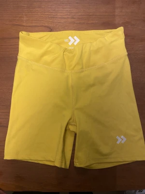 Gula cykelshorts från Lager 157 - Snygga gula cykelshorts från Lager 157 med hög midja och stretchigt material. Perfekta för träning eller sportaktiviteter. Lager 157 -logga framtill. Sköna och flexibla för rörelse.