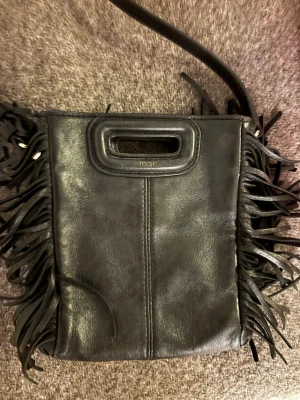 Svart Maje väska  - Cool svart handväska i läder från Maje med fransar längs sidorna och både axelrem och handtag. Bra skick, ser grå ut på bilderna men är svart.