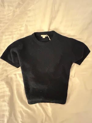 Mörkblå stickad kortärmad topp - En enkel och stilren mörkblå stickad topp med korta ärmar och rund hals. Modellen är något croppad och passar perfekt till jeans eller kjol. 