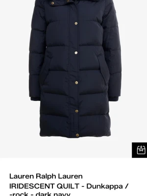 Mörkblå lång dunjacka kappa  Lauren Ralph Lauren Stl s  - Snygg mörkblå lång dunjacka från Lauren Ralph Lauren med huva och fuskpälsdetalj. Jackan har guldfärgade knappar, två snedställda fickor. Perfekt för kalla vinterdagar och riktigt varm. Det har släppt några trådar på fickan, syns knappt men ska veta om