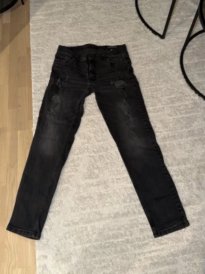 DSQUARED2 jeans - Säljer ett par svarta slim fit jeans från Dsquared 2 med slitningar och hål på framsidan. Jeansen har klassisk femficksdesign och en snygg tvättad look. Perfekta för dig som gillar en lite tuffare stil.