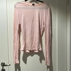 Ljusrosa långärmad topp - En enkel och stilren ljusrosa långärmad topp med rund halsringning. Toppen är tunn och har en smickrande passform som passar perfekt till jeans eller kjol. Materialet känns mjukt mot huden och färgen är superfin till både vår och sommar.