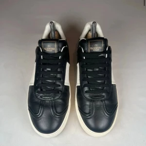 Valentino flycrews  - Svartvita Valentino Garavani sneakers i skinn med klassisk låg profil och rund tå. Snygga nitar på sulan ger extra edge. Svarta snören och vit sula. Kommer med original dustbag. Nypris ligger runt 8000kr vårt pris är 2299kr en super deal!!De är storlek 39 men de passar 40,5 och 40