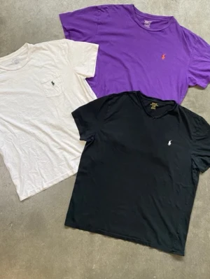 3-pack t-shirts från Ralph Lauren - Tre klassiska t-shirts från Ralph Lauren i svart, vitt och lila. Alla har kort ärm och rund halsringning, med den ikoniska broderade loggan på bröstet. Den vita t-shirten har dessutom en bröstficka. Perfekta basplagg för garderoben.