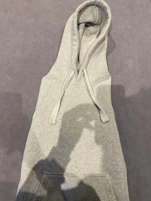 Ljusgrå hoodie med huva och ficka - En stilren ljusgrå hoodie med huva och dragsnören. Hoodien har en klassisk känguruficka framtill och ribbade muddar vid ärmar och nederkant. Tillverkad i mjukt sweatshirtmaterial, perfekt för en avslappnad look.