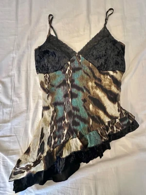 Leopardmönstrat linne med spets - Säljer ett linne i loungewear-stil med leopardmönster i brunt, svart och grönt. Överdelen har svarta spetsdetaljer och tunna axelband. Nederdelen har en asymmetrisk volangkant som ger en cool och unik look. Perfekt för chill dagar hemma.