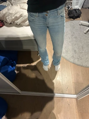 Ljusblå bootcut jeans med dubbla knappar - Säljer ett par ljusblå bootcut jeans med låg/medel midja och dubbla knappar i midjan. Jeansen har klassisk femficksdesign och är tillverkade i stretchigt denimtyg för en bekväm passform. Perfekta för en avslappnad och trendig look.