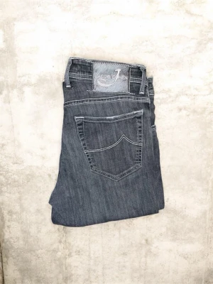 Grå jeans från Jacob Cohen - Snygga grå jeans från Jacob Cohen med raka ben och klassisk femficksdesign. Jeansen har tydliga vita sömmar och en patch med logga bak i midjan. Perfekta för en stilren och avslappnad look.