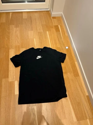 Svart Nike T-shirt loose fit  - Snygg svart T-shirt från Nike med klassisk vit logga på bröstet. Modellen är loose fit för en avslappnad vibe och passar perfekt till streetwear-stilen. Tillverkad i mjuk bomull för skön känsla hela dagen. Hör av dig vid frågor!