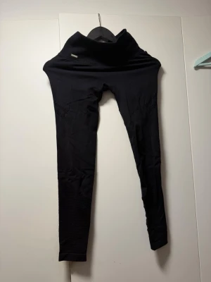 Svarta seamless leggings med meshdetaljer - Svarta träningsleggings med hög midja och seamless design. Snygga meshdetaljer längs benen ger en sportig look. Perfekta för träning eller chill. Stretchigt material som sitter skönt och följer kroppen.