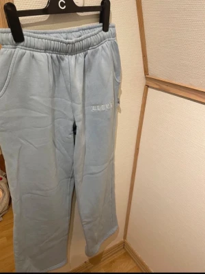 Ljusblå mjukisbyxor HOOKED - Säljer ett par ljusblå mjukisbyxor med broderad text 'HOODRICH bak och 'HOODRICH' fram. Byxorna har resår i midjan och raka ben. Perfekta för chill dagar och har en skön, mjuk känsla. Materialet är fleece-liknande och riktigt cozy.