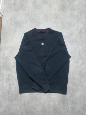 Mörkblå sweatshirt från Hugo - Mörkblå sweatshirt från Hugo med rund halsringning och diskret logotyp på bröstet. Tröjan har ribbade muddar vid ärmslut och nederkant samt en klassisk, avslappnad passform. Perfekt för en clean och stilren look.