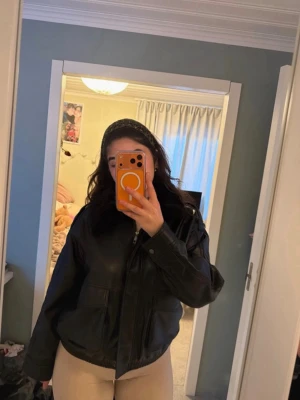 Svart oversized skinnjacka - Snygg svart oversized skinnjacka med dragkedja framtill och breda ärmar. Jackan har två stora fickor och en klassisk krage. Perfekt för dig som gillar en trendig och avslappnad stil.