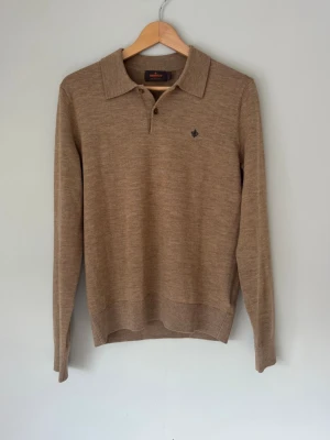 Beige merinoullströja från Morris - Klassisk beige långärmad tröja från Morris i 100% merinoull. Tröjan har pikékrage med två knappar och en liten broderad logga på bröstet. Perfekt för dig som gillar stilrena och tidlösa plagg med en mjuk och skön känsla.