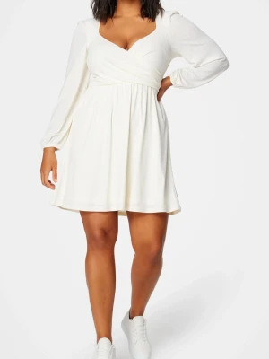 Vit omlottklänning med lång ärm - Superfin vit kortklänning med omlott över bysten och v-ringad hals. Klänningen har långa ärmar med lätt puff och resår vid ärmslut. Tillverkad i ett mjukt och lätt material som ger ett snyggt fall. Perfekt för dig som tar studenten! OBS! Hade en säkerhetsnål vid bysten då v-ringingen föll väldigt långt ner när man hoppade och firade, vilket gjorde att den blev lite nopprig vid bysten. Det syns på dom två sista bilderna. Det är dock inget man ser på långt håll.