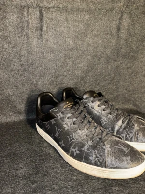 Louis vuitton Stl 45  - Snygga svarta sneakers från Louis Vuitton med klassiskt monogrammönster i grått. Skorna har lågt skaft, svarta skosnören och vit sula. Tillverkade i läder med exklusiv känsla och detaljer i guld på tungan. Storlek 45 men passar mer 44.5 skulle jag säga. Lite creesade därav priset. Köpta hos garmsmarket för något år sen för 3800kr kvitto finns via mail. 