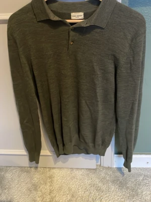 Olivgrön långärmad pikétröja John Henric - Snygg olivgrön långärmad pikétröja från John Henric. Tröjan har klassisk krage, två knappar framtill och ribbade muddar vid ärmslut och nederkant. Perfekt för en stilren och avslappnad look.hål i ena armen kolla bild. 