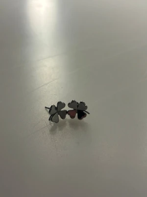 Fyra-blads örhängen i silverfärg - Snygga örhängen i form av fyrklöver med metallic silverfärg och inslag av roséguld. De har en enkel och stilren design som passar till många olika looks. Perfekta för dig som gillar subtila men unika accessoarer.