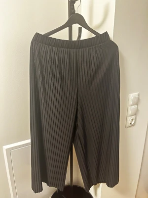 Svarta plisserade byxor från Monki - Säljer ett par svarta byxor från Monki i storlek XS. Byxorna har plisserad design, bred resår i midjan och är tillverkade i ett mjukt, flowy material som ger en avslappnad och trendig look. Perfekta för dig som gillar bekväma men snygga byxor.