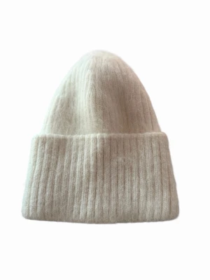 Vit ribbstickad mössa i ullmix - Mysig vit mössa med bred uppvikt kant och ribbstickat mönster. Tillverkad i en mjuk ullmix som ger en fluffig och varm känsla. Perfekt för kalla dagar och enkel att matcha med olika outfits.