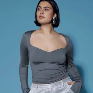 Grå långärmad topp från Gina Tricot - Snygg grå långärmad topp från Gina Tricot med djup v-ringning och figurnära passform. Perfekt för att lyfta vilken outfit som helst med sin stilrena design och trendiga snitt.