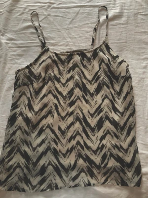 Vero Moda linne med mönster - Snygg svartvit linnetopp från Vero Moda med zigzag-mönster och tunna axelband. Perfekt för sommaren. Lätt och luftig känsla.