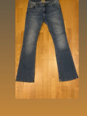 Blå bootcut jeans - Snygga blå lågmidjade bootcut jeans med ljusa slitningar och en broderad lilja på myntfickan. Jeansen är från Morris, deras damkollektion. Storlek 30/32💞