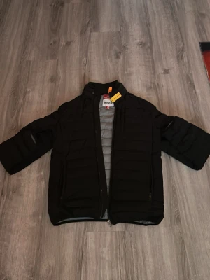 Svart dunjacka från Parajumpers - Snygg svart dunjacka från Parajumpers med ståkrage och dragkedja framtill. Jackan har två sidofickor med dragkedja och en gul detalj vid halsen. Perfekt för kalla vinterdagar och riktigt stilren design. Ps jackan har en lagningslapp på ryggen eftersom det råka gå sönder lite men det är inget som man tänker på! Hör av er/Alfred