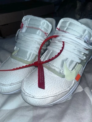 Nike x Off-White vita sneakers - Säljer ett par vita Nike x Off-White sneakers med mesh- och syntetmaterial, ikonisk Off-White zip-tie i rött och detaljer som genomskinlig swoosh och orange tag. Skorna har Off-White logga på innersulan och unika sömmar på plösen.