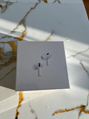 Apple AirPods Pro (2nd generation) - Trådlösa in-ear hörlurar från Apple i vit färg. AirPods Pro (2nd generation) har en stilren och kompakt design med silikonproppar för bättre passform och brusreducering. Perfekta för musik, samtal och gaming. Levereras i originalförpackning.