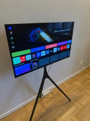 LG smart-TV på stativ - Säljer en modern LG smart-TV med tunn svart ram och stilrent stativ i metall. TV:n har stor skärm och smarta funktioner som appar för Netflix, YouTube och fler streamingtjänster. Perfekt för gaming, film och serier. Snygg design som passar in i alla rum.  Ny pris 14999 använd i ca 5-6 månader finns i Norrköping 