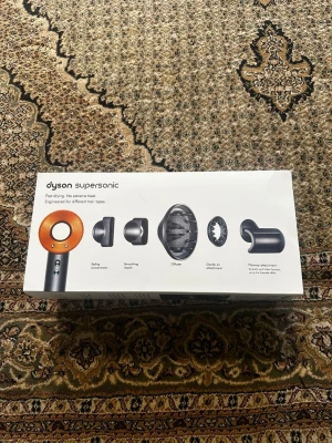 Dyson Supersonic hårfön orange - Säljer en Dyson Supersonic hårfön i orange och grått. Medföljer flera munstycken: stylingkoncentrator, smoothing nozzle, diffuser, gentle air och flyaway attachment. Perfekt för olika hårtyper och enkel att använda tack vare smart design.