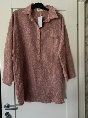 Hängmatta - Luftig rosa blus från Signature med crinkle-effekt, klassisk krage och knappslå framtill. Blusen har en bröstficka och trekvartsärm. Perfekt för en avslappnad och trendig look.