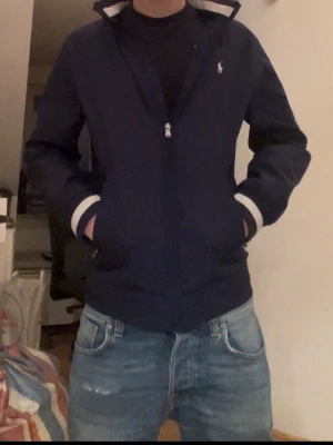 Mörkblå bomberjacka med vita muddar - Snygg mörkblå bomberjacka med vita muddar vid ärmslut och midja. Jackan har dragkedja framtill och två sid Native fickor. Inbyggd luva syns på fjärde bilden. Den är på gränsen till för liten för mig på bilen och jag är ca 172. Pris kan diskuteras. Skriv vid frågor!