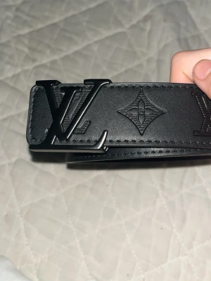 Svart skärp i skinn - Snyggt svart skärp från i soprent skinn. Bältet har präglade monogramdetaljer längs hela bandet och en stilren look som passar till det mesta. Perfekt accessoar för att lyfta din outfit.