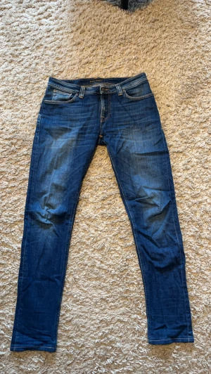 Mörkblå jeans från Nudie - Säljer ett par mörkblå jeans från Nudie Jeans med klassisk femficksmodell och snygga slitningar.  Sjukt snygg tvätt storlek 32/34 
