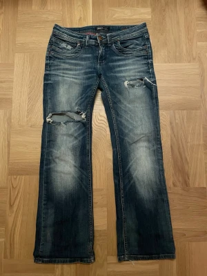 Blå slitna bootcut jeans från ONLY - Snygga blå bootcut jeans från ONLY med slitningar och hål på båda benen. Jeansen har klassisk femficksdesign, låg midja och tydliga slitningar för en trendig look. Perfekta för dig som gillar en avslappnad och cool stil. Tyvärr har dom gått sönder lite där bak under rumpan men det är ingenting man tänker på 