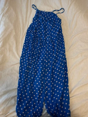 Blå prickig långklänning med smala band - Blå långklänning med vita prickar och smala axelband. Klänningen har en avslappnad passform och ärmlös design, perfekt för sommardagar. Tillverkad i ett lätt material som ger en luftig känsla.