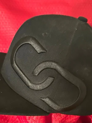 Svart keps flexfit cap 56cm  - Snygg svart keps med en stor, upphöjd 3D-logga framtill. Kepsen har klassisk form med böjd skärm och är tillverkad i ett slitstarkt tygmaterial. Perfekt för dig som gillar stilrena accessoarer med en modern touch.