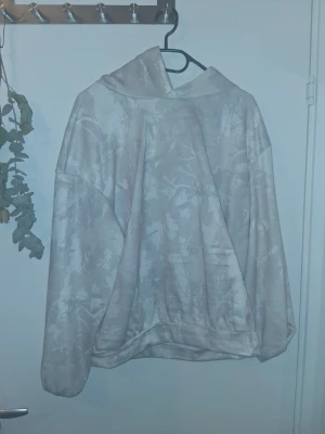 Beige hoodie med mönster - Säljer en beige hoodie med diskret mönster i ljusare toner. Hoodien har en stor huva och avslappnad passform, perfekt för en chill och stilren look. Materialet känns mjukt och bekvämt mot huden. Inga synliga loggor eller märken.