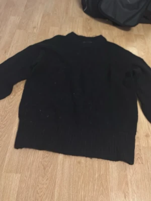 Svart stickad tröja med rund hals - En enkel svart stickad tröja med rund hals och långa ärmar. Tröjan har ribbstickade muddar vid ärmslut och nederkant. Perfekt för lager-på-lager och passar till det mesta i garderoben.