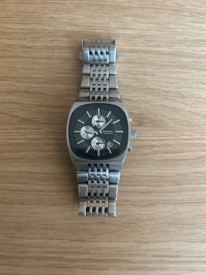 Diesel silverfärgad klocka - Stilren klocka från Diesel i silverfärgat metallarmband och fyrkantigt svart ur med tre mindre urtavlor. Snygg och modern design med tydliga vita markeringar och robust känsla. Perfekt accessoar för dig du vill sticka ut.